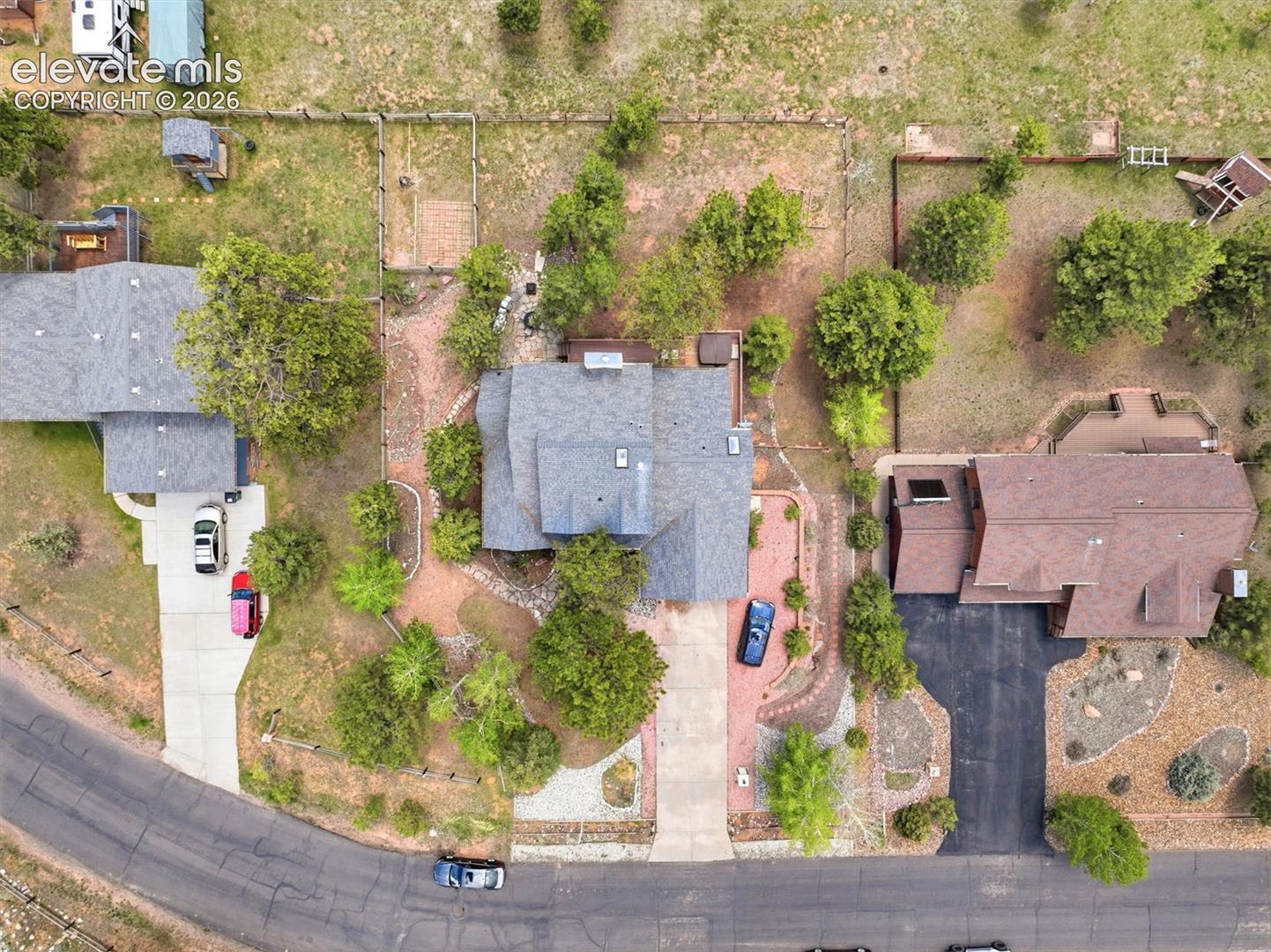 Central property featuring a gray shingle roof, paved driveway, and mature landscaping