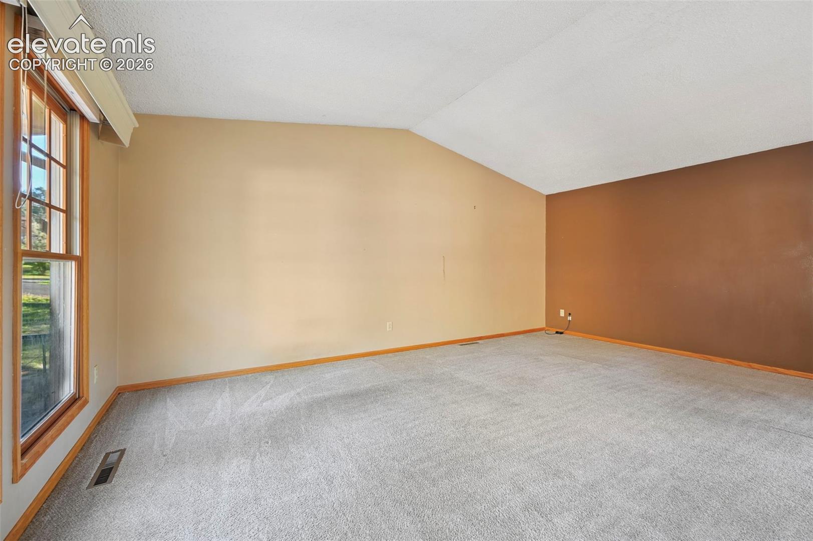 Vaulted ceiling with an accent wall, wall-to-wall carpeting, and wood-framed window