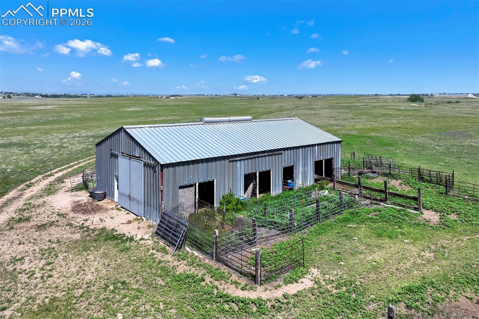 Agricultural outbuilding featuring a corrugated metal roof and siding, multiple entry points, and surrounding fenced areas