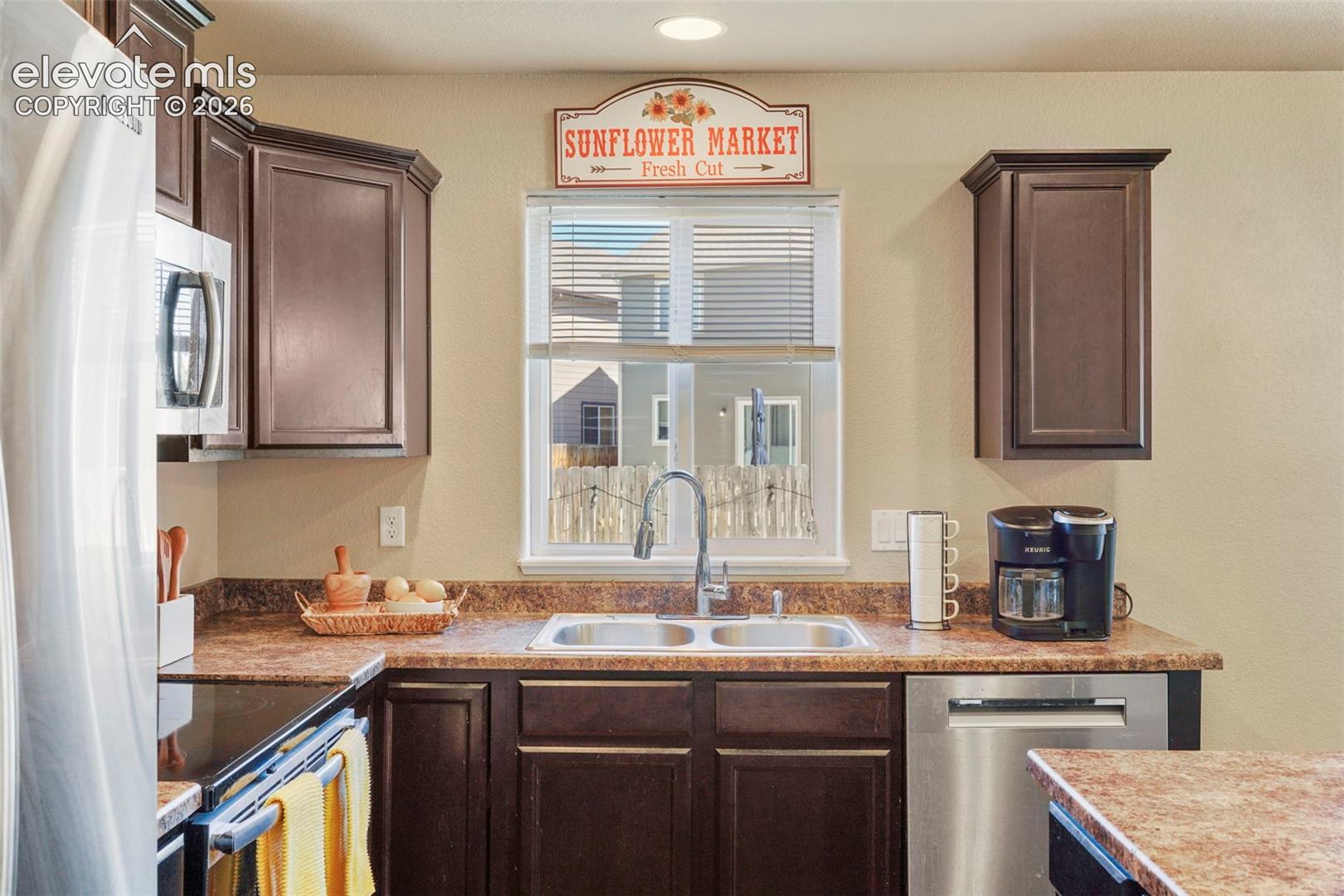 Dark wood-finish cabinetry, stainless steel dishwasher, stainless steel sink with a gooseneck faucet, window with blinds, and recessed lighting