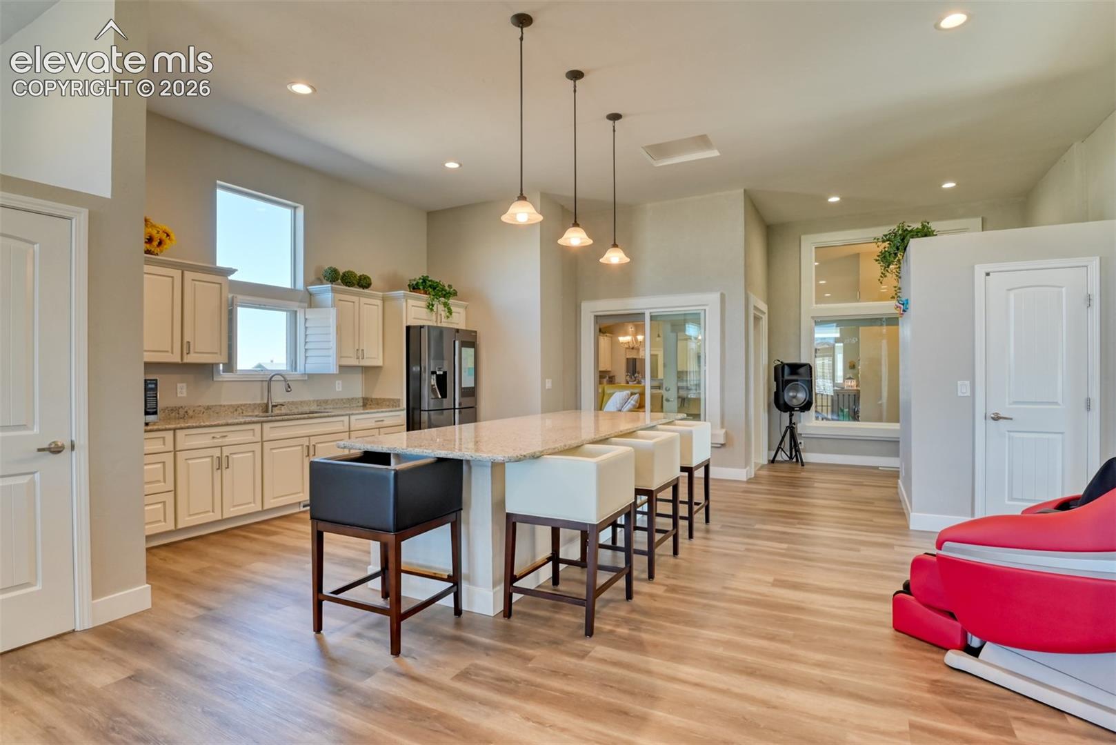 Family room area featuring wood-finish flooring, a kitchenette with light cabinetry, granite countertops, and recessed lighting.