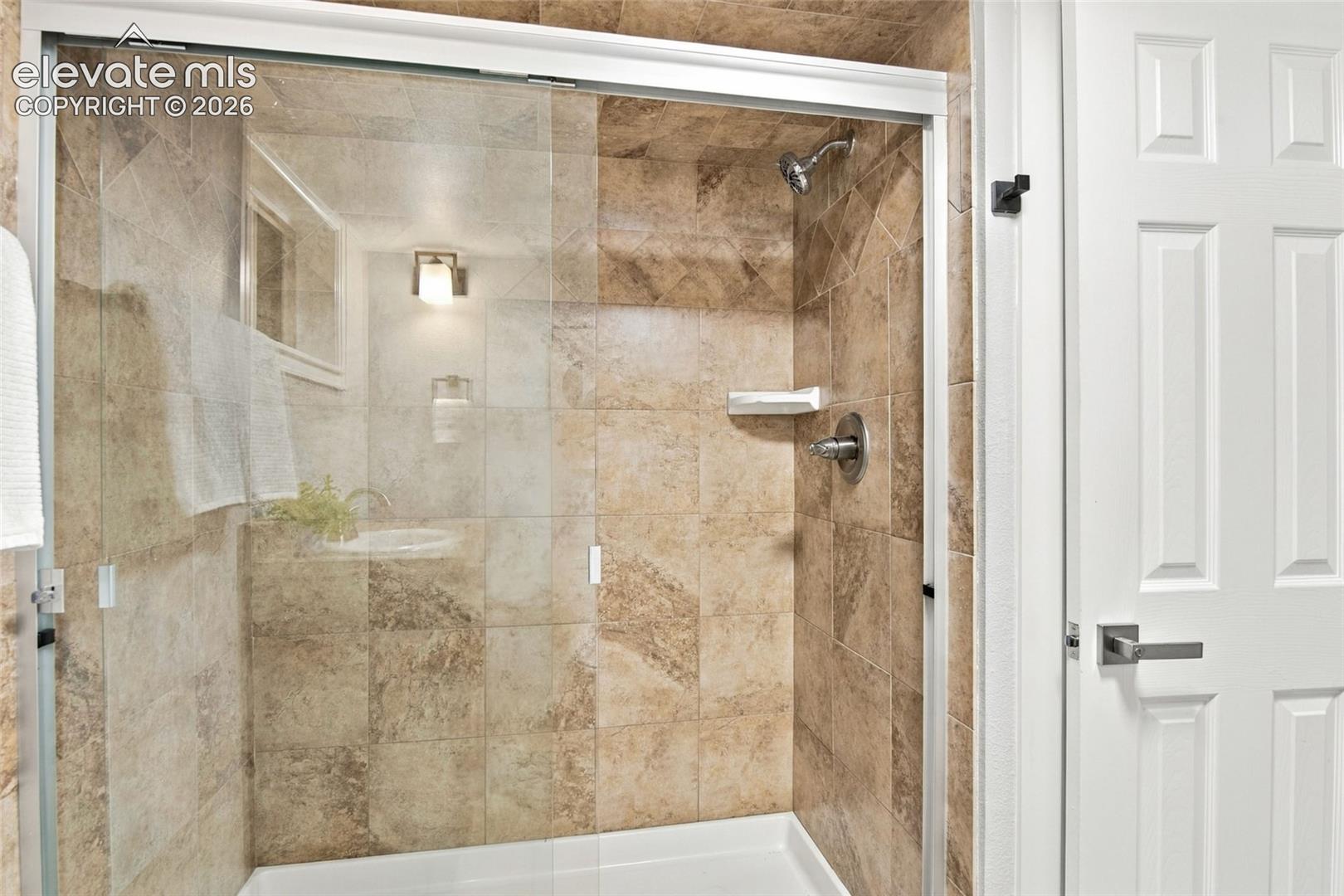 Walk-in shower featuring floor-to-ceiling stone-look tiling, a glass enclosure, an integrated shelf, and chrome plumbing fixtures