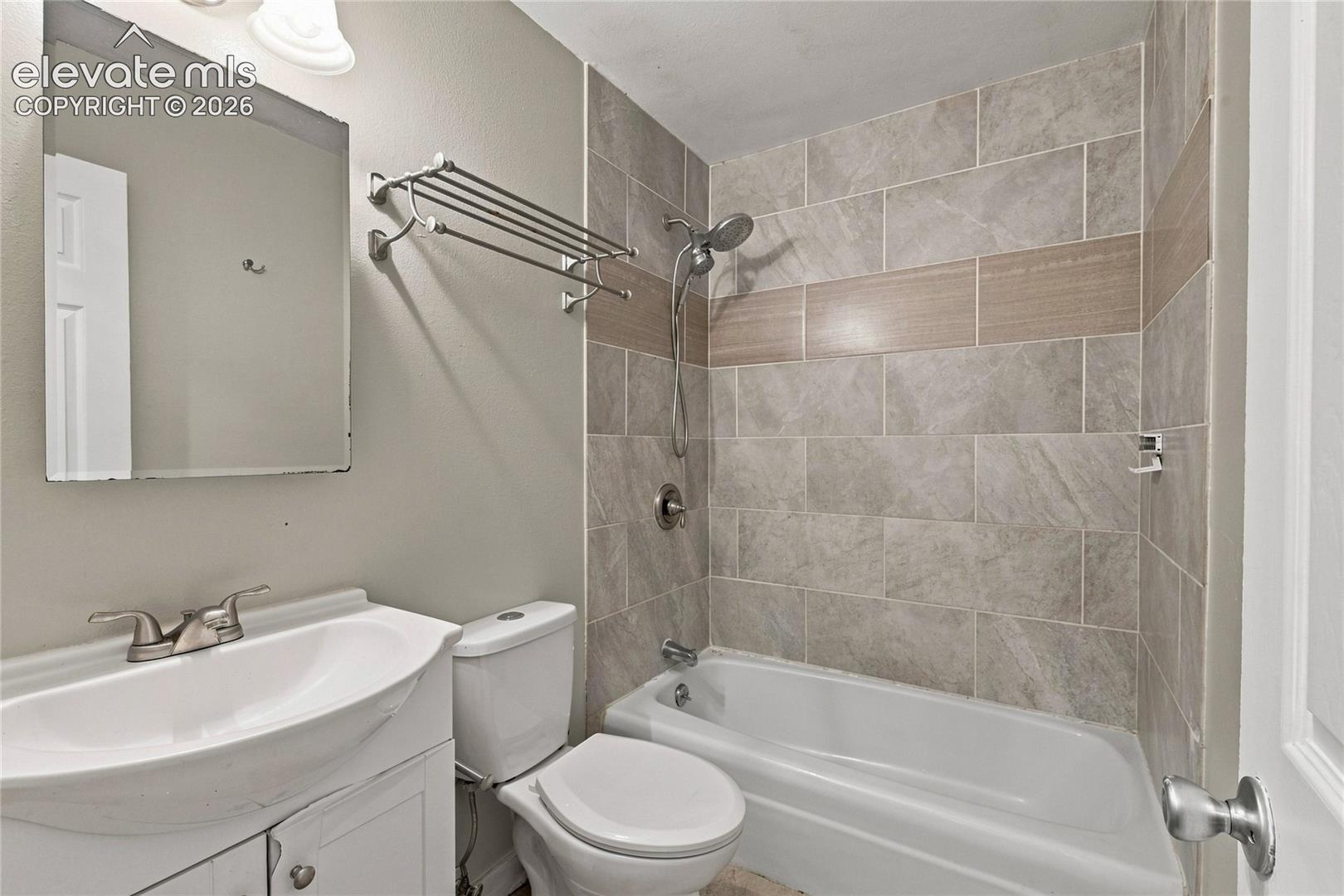 Bathroom with a white vanity sink, brushed nickel faucet, wall-mounted mirror, and a tiled shower-tub combination