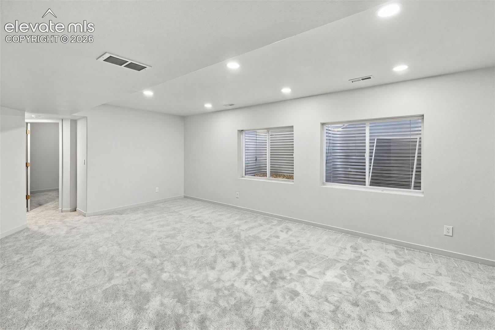 Neutral interior space featuring wall-to-wall carpeting, recessed ceiling lighting, and egress window wells with metal corrugated siding