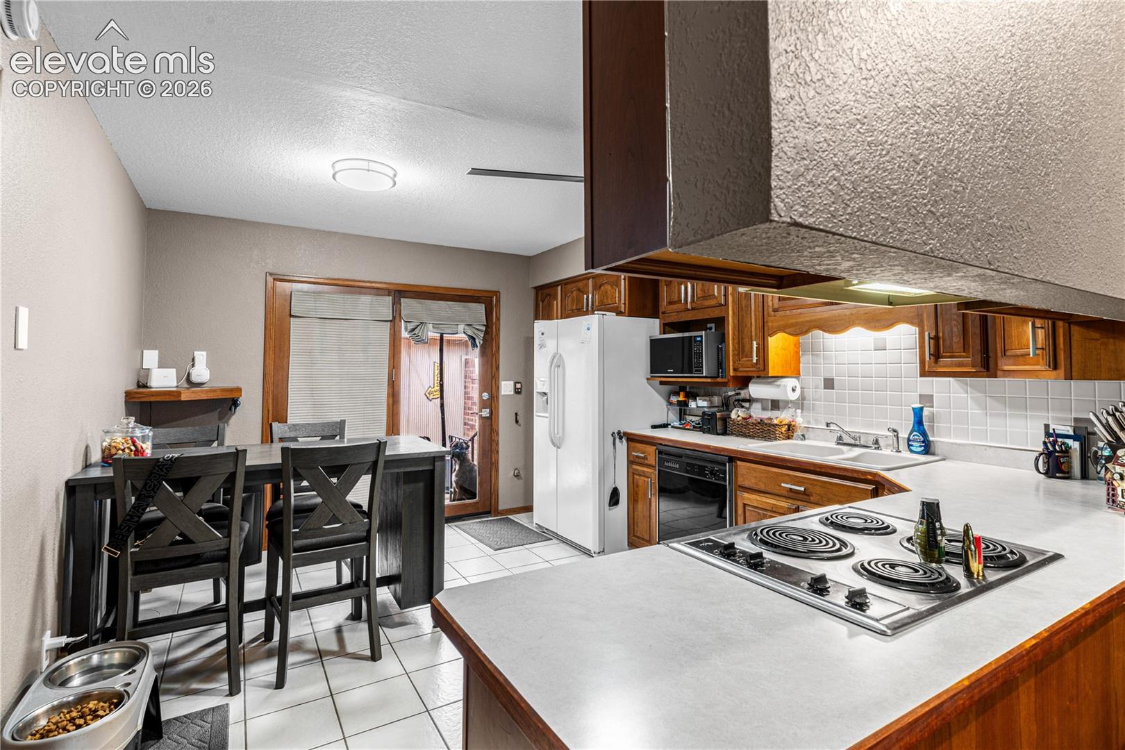 Kitchen featuring stained wood cabinetry, white tile backsplash, a drop-in electric cooktop, and a double-basin sink