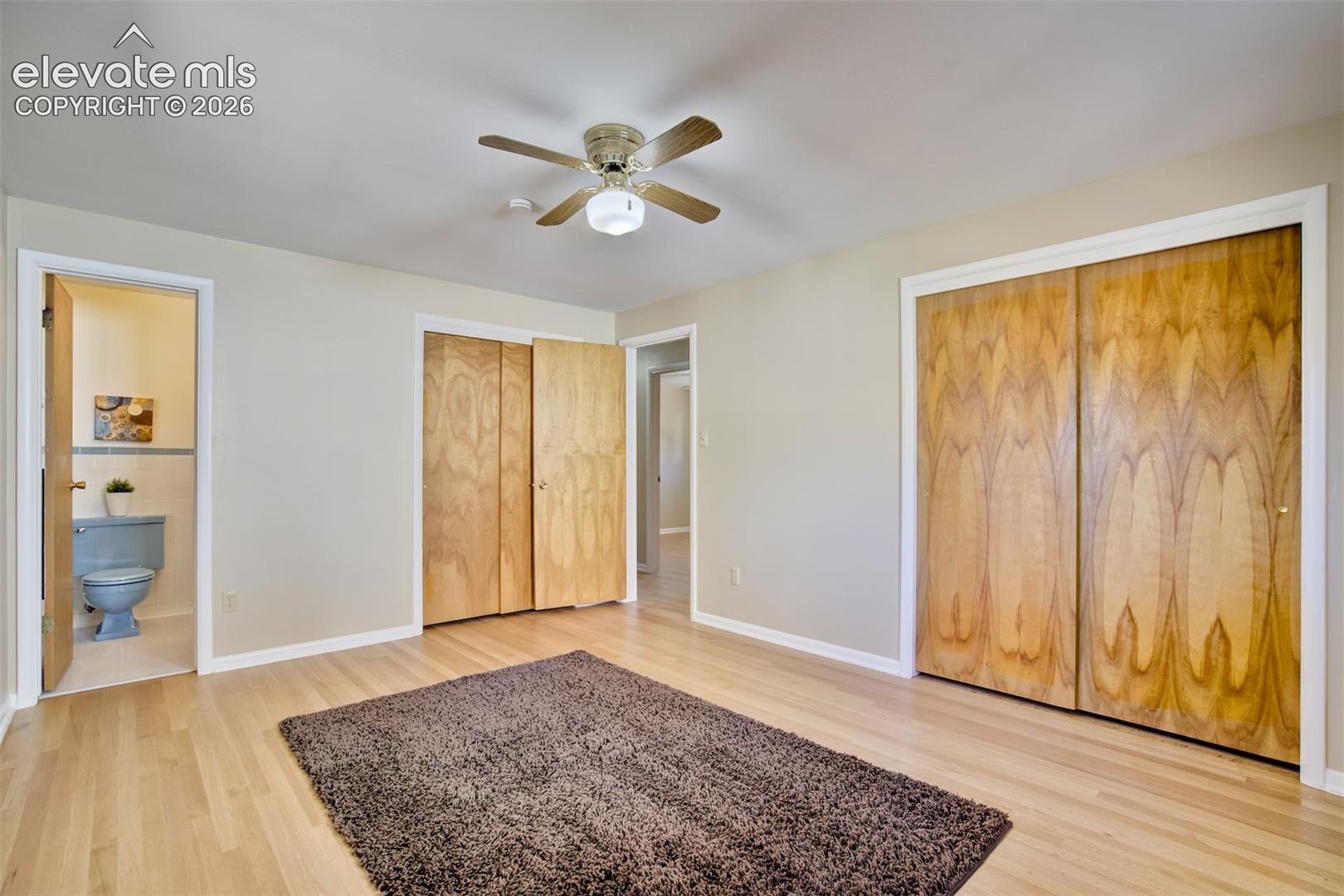 Wood-finish flooring, dual built-in closets with wood-grain doors, and a ceiling-mounted light fixture with a fan