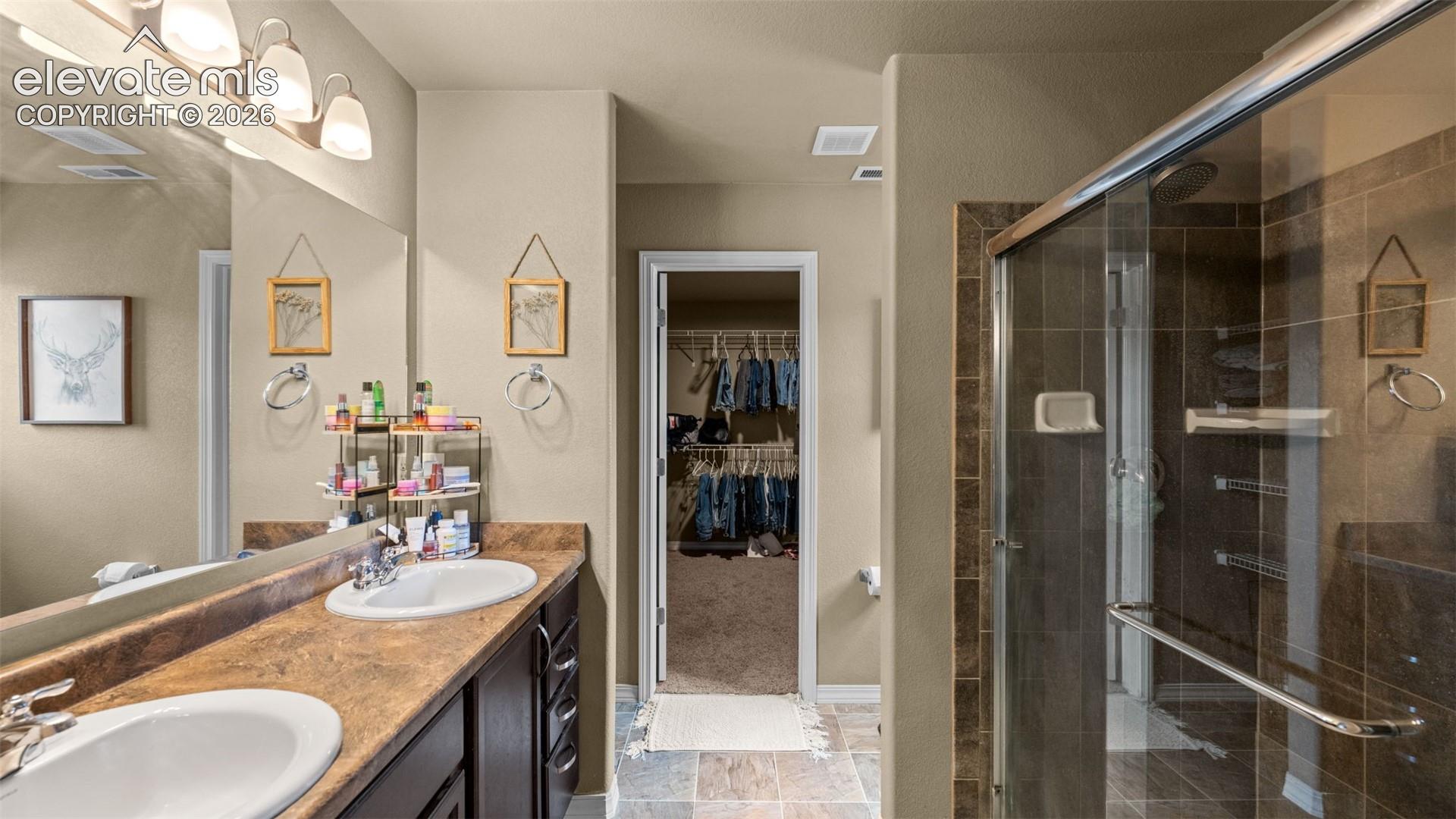 Bathroom featuring a double vanity with integrated sinks, a sliding glass shower enclosure, and a walk-in closet with built-in shelving