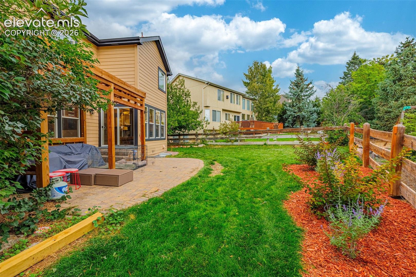 Expansive backyard featuring a manicured lawn, wood fencing, and landscaped garden beds