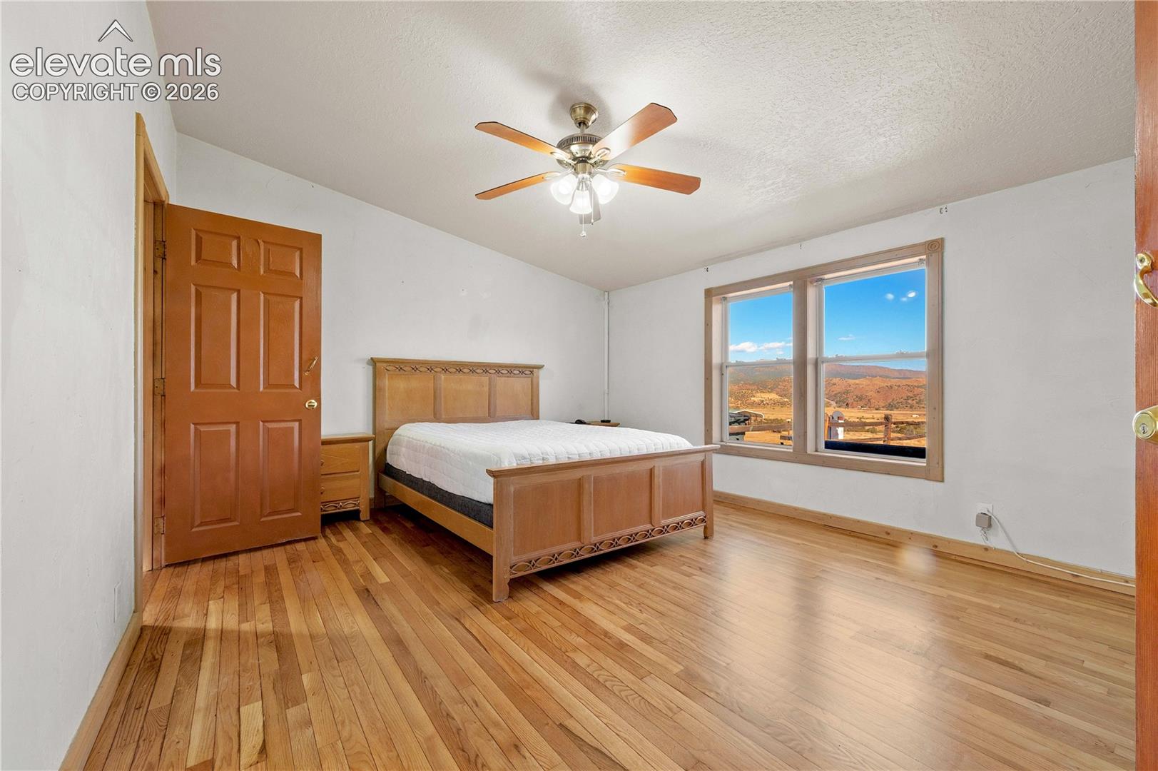 Bedroom with vaulted ceiling, a textured ceiling, light hardwood / wood-style floors, and ceiling fan