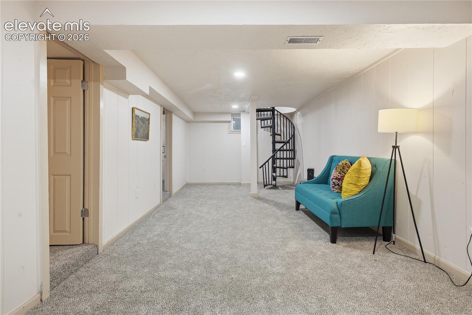 Interior space featuring neutral carpeting, a black metal spiral staircase, recessed lighting, and a paneled interior door