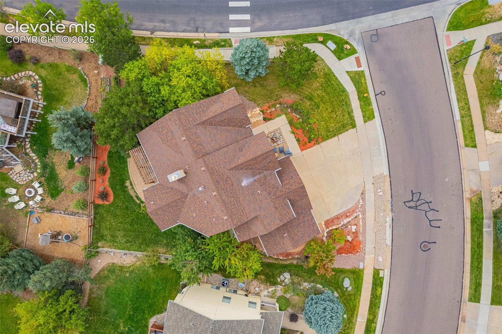 L-shaped asphalt driveway, brown shingle roof, mature landscaping, paved sidewalks, and asphalt roadways