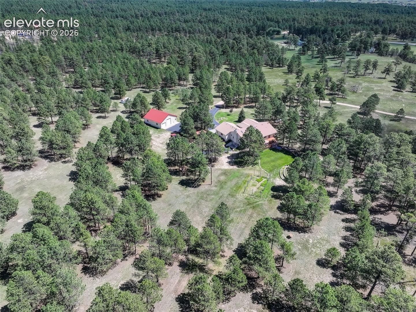 Aerial view of property with landscaped back yard, fenced garden, RV workshop, and mature trees. 