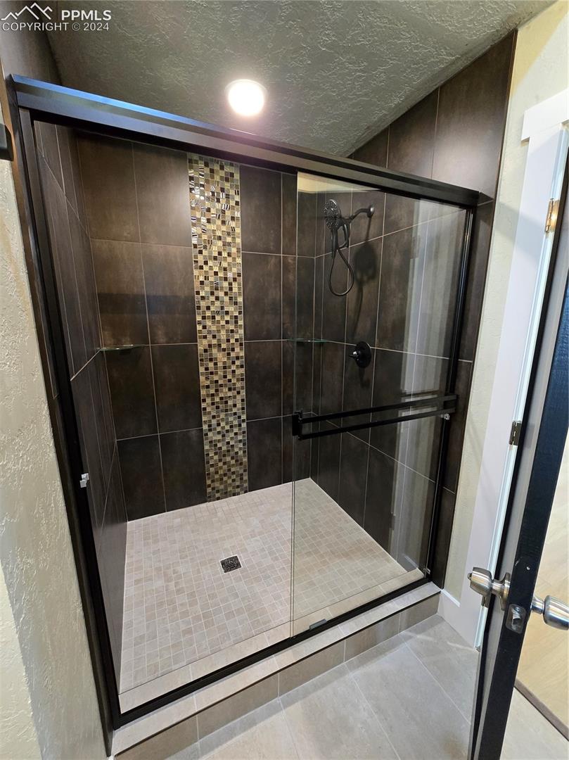 Bathroom with a shower with door, tile patterned floors, and a textured ceiling