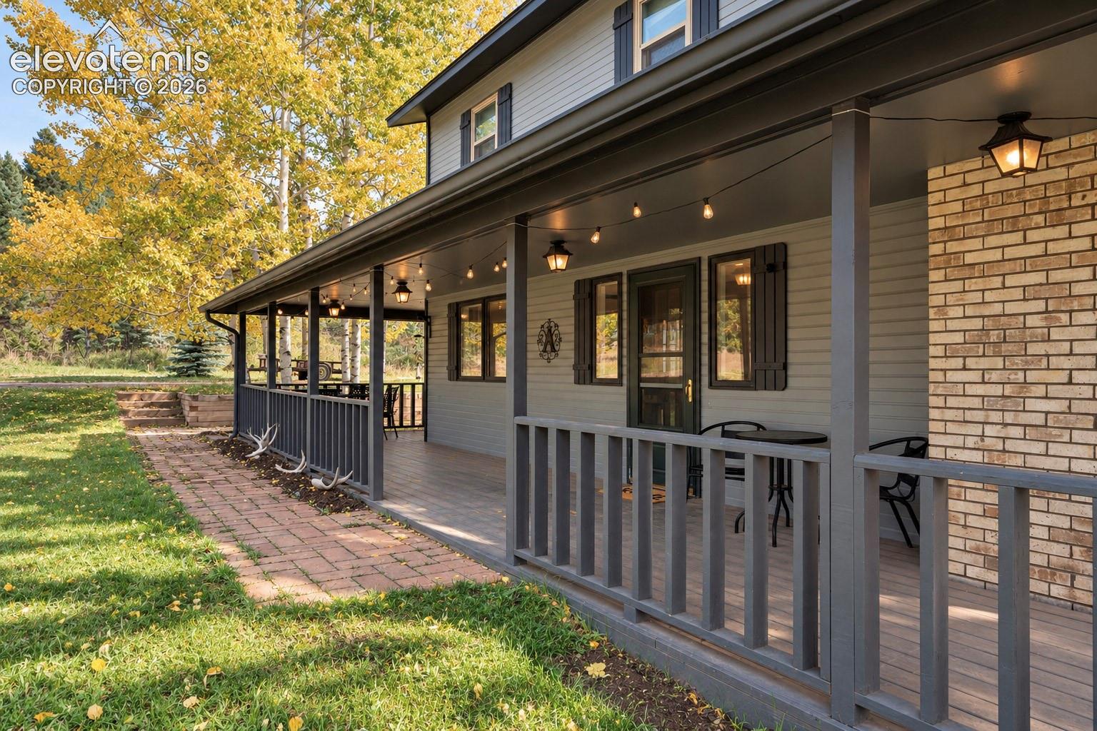 Expansive covered porch with a wood-finish deck, brick accent siding, and classic railings