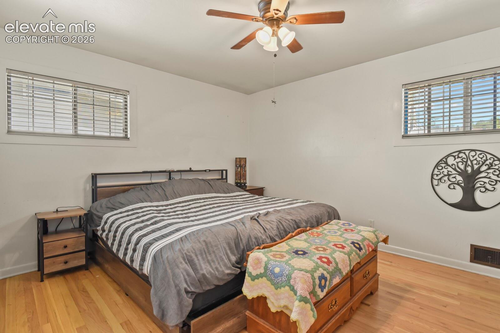 Hardwood-finish flooring, two windows with horizontal blinds, and a ceiling fan with integrated lighting