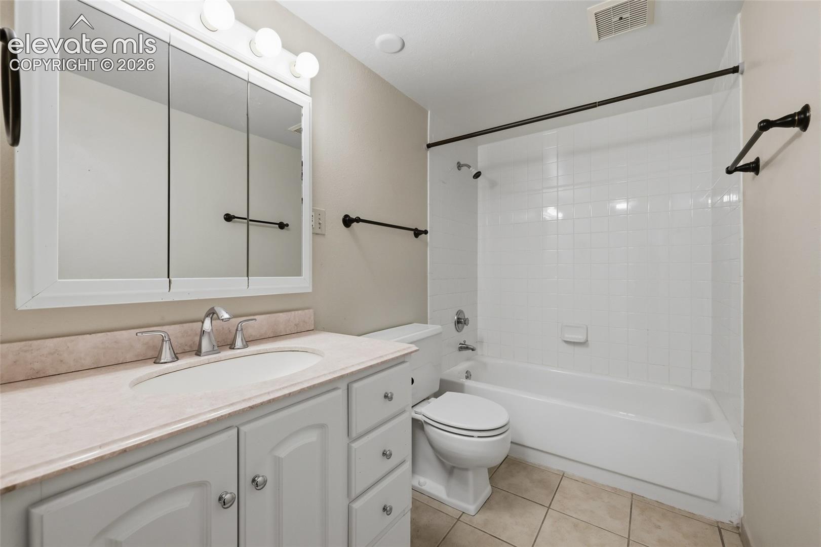 Bathroom featuring a white vanity cabinet with a solid surface countertop, an oval undermount sink, a tri-fold medicine cabinet, and a bathtub with a tiled surround