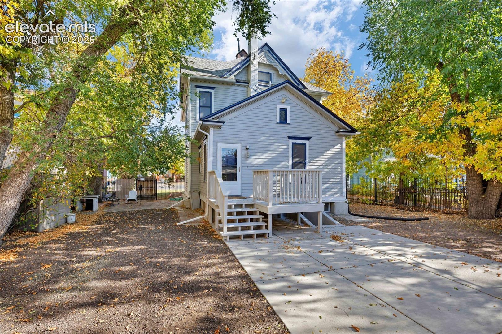 Two-story residence featuring light-toned horizontal siding, a gabled roofline, a raised wooden deck with railings, and a paved concrete driveway