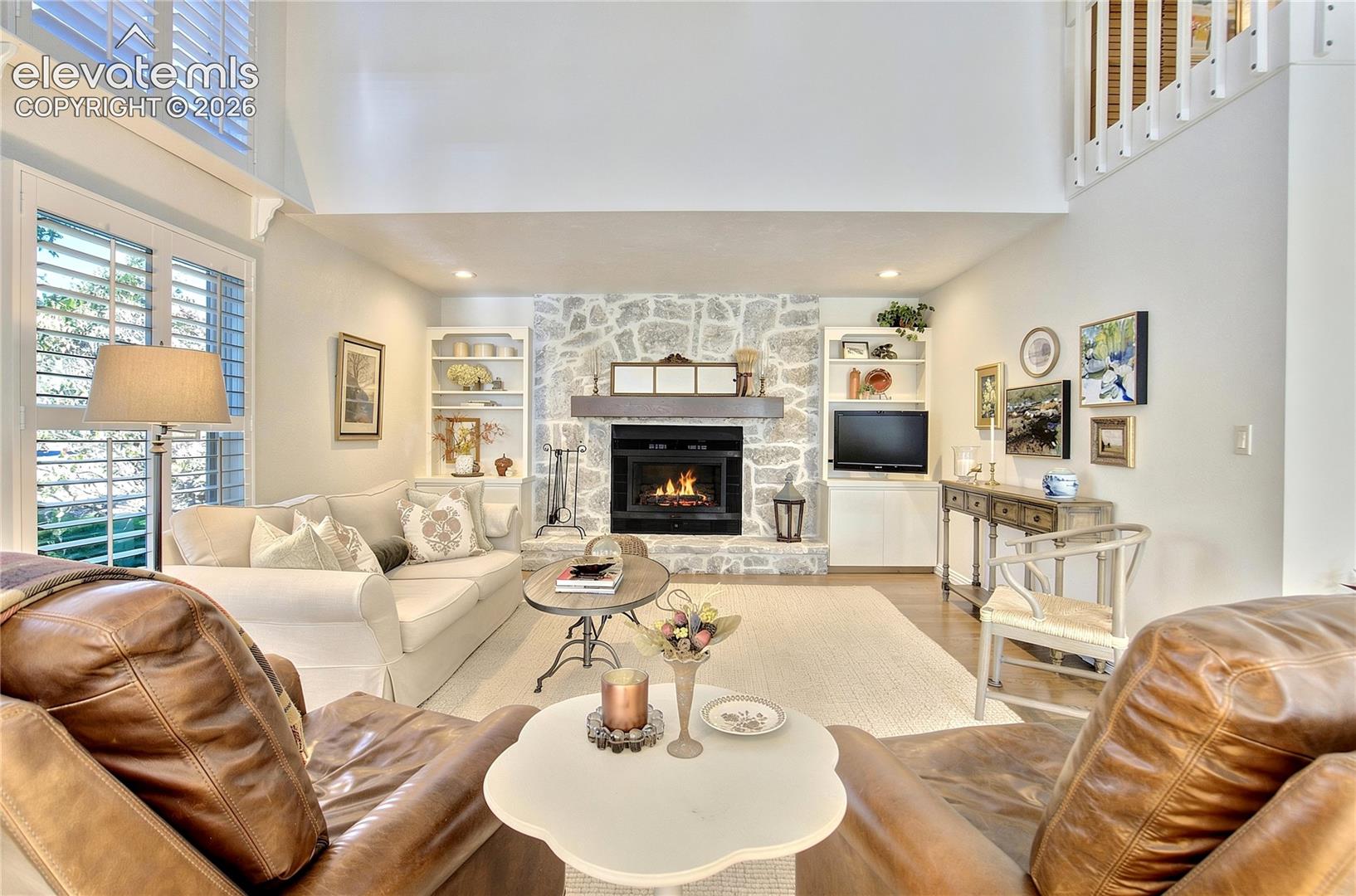 A stone-surround wood-burning fireplace flanked by built-ins creates a striking focal point within the grand space.