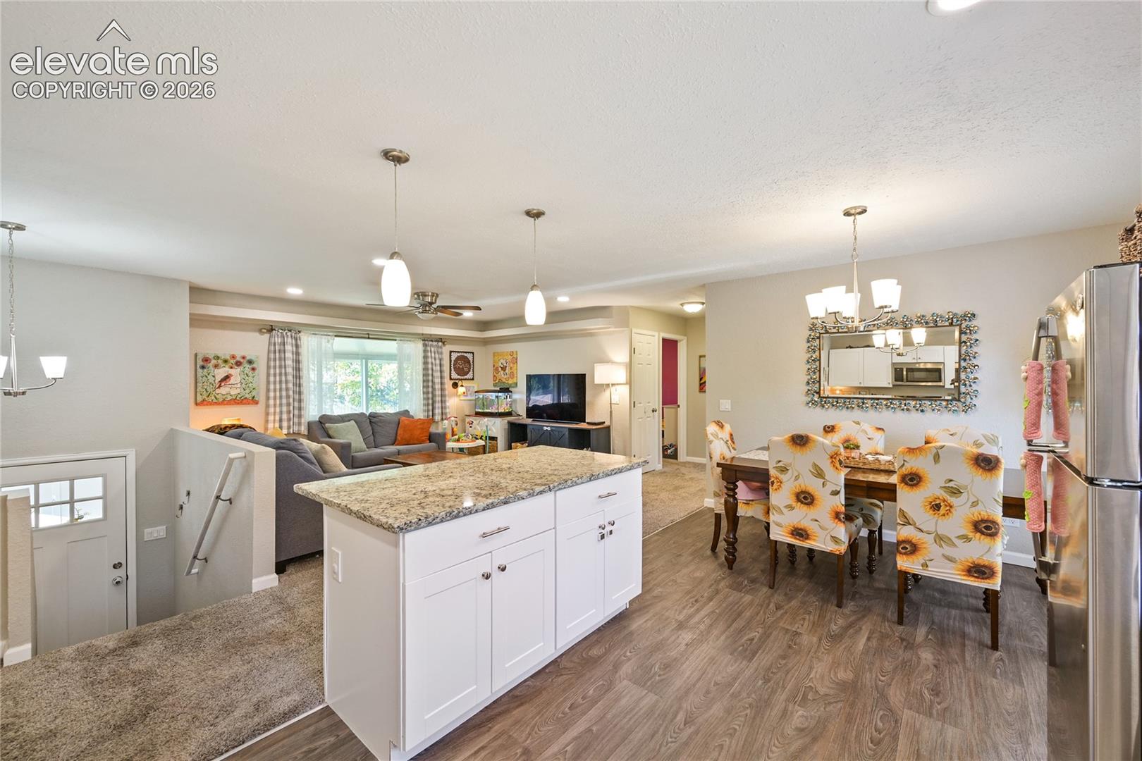 Kitchen island with stone countertop, white shaker-style cabinetry, wood-finish flooring, and multi-light pendant fixtures
