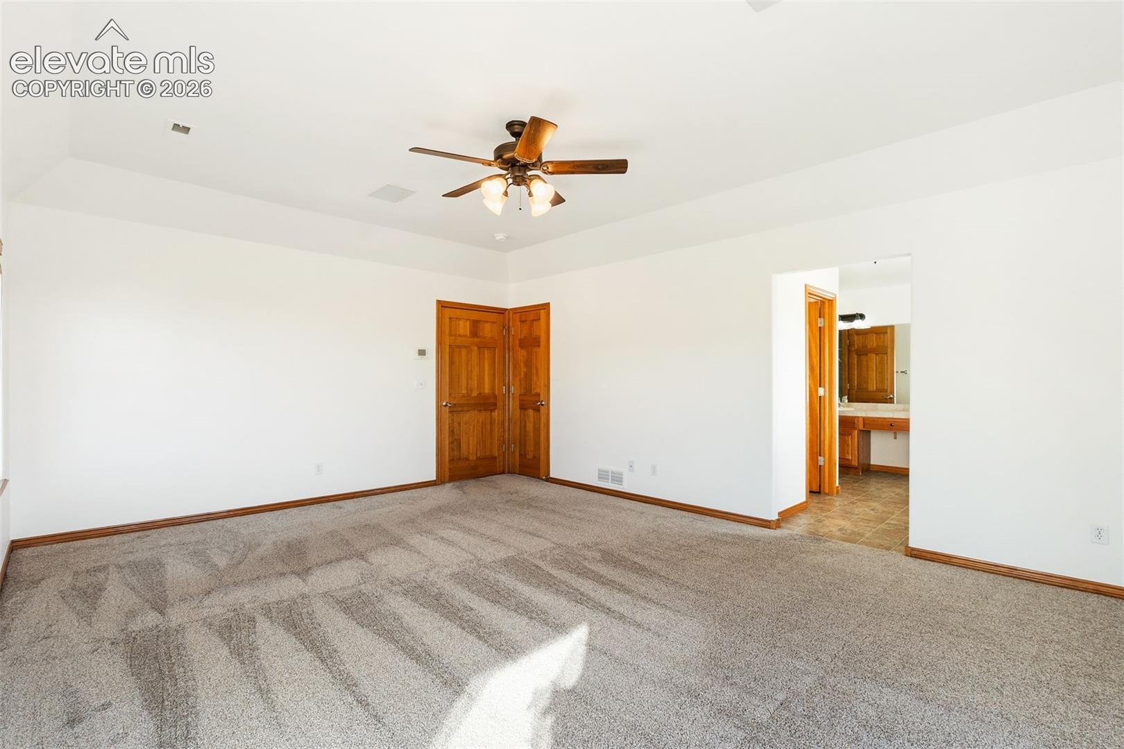 Tray ceiling, carpeted flooring, multi-blade ceiling fan with integrated lighting, and natural wood-finish interior doors