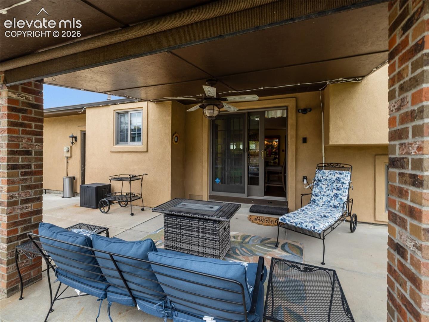 Covered patio with a ceiling fan, concrete flooring, brick columns, and a sliding glass door