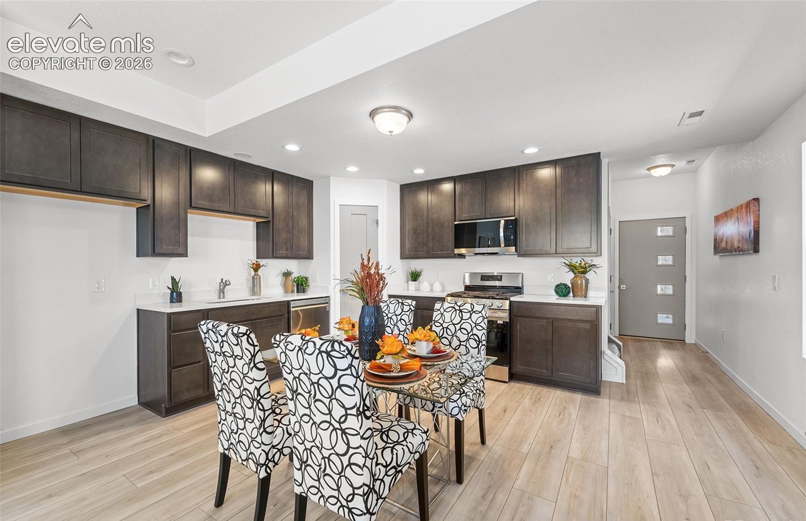 Kitchen featuring dark wood-finish cabinetry, stone-style countertops, stainless steel appliances, recessed lighting, and wood-finish flooring