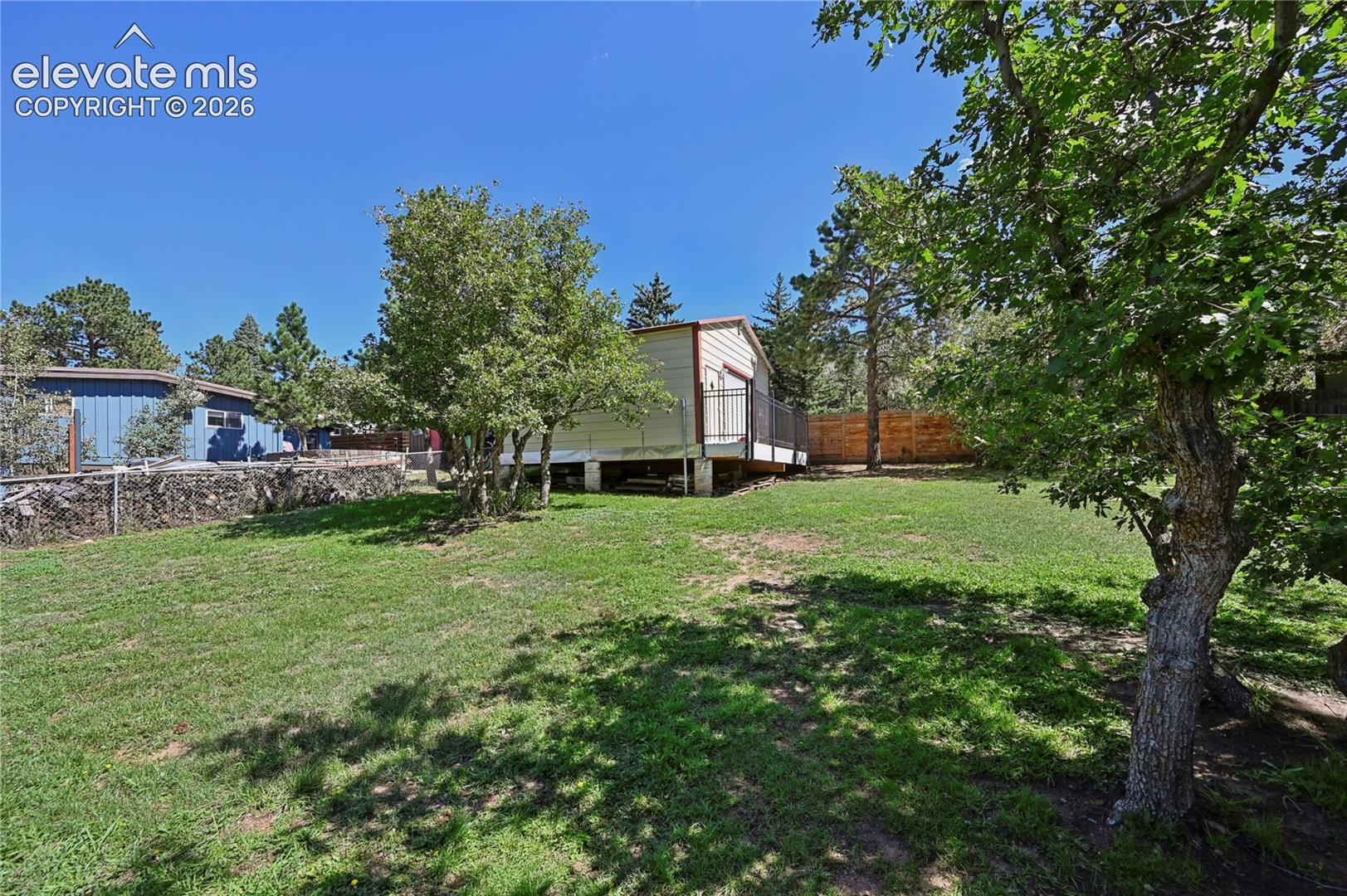 Expansive grassy yard with mature trees and a detached structure featuring a side deck with railing