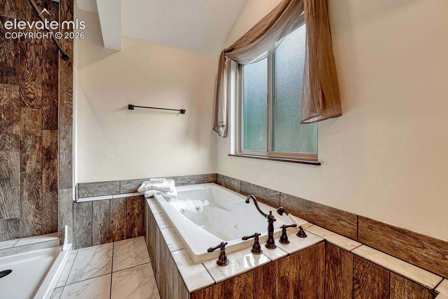 Jetted soaking tub featuring wood-finish tile surround, oil-rubbed bronze deck-mounted faucet, and a dual-pane frosted window