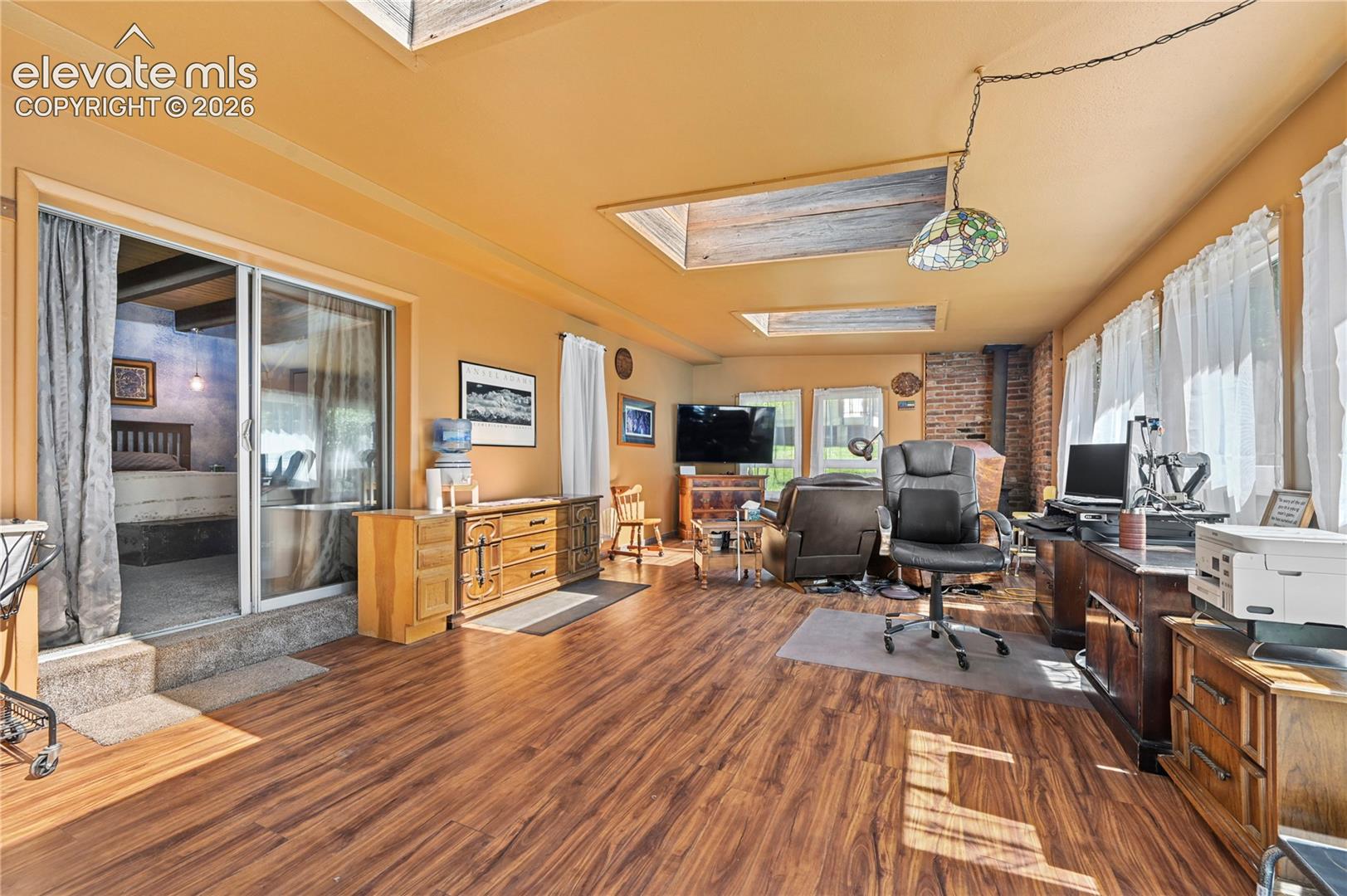 Wood-finish flooring, multiple skylights, brick chimney feature, and a sliding glass door to an additional space