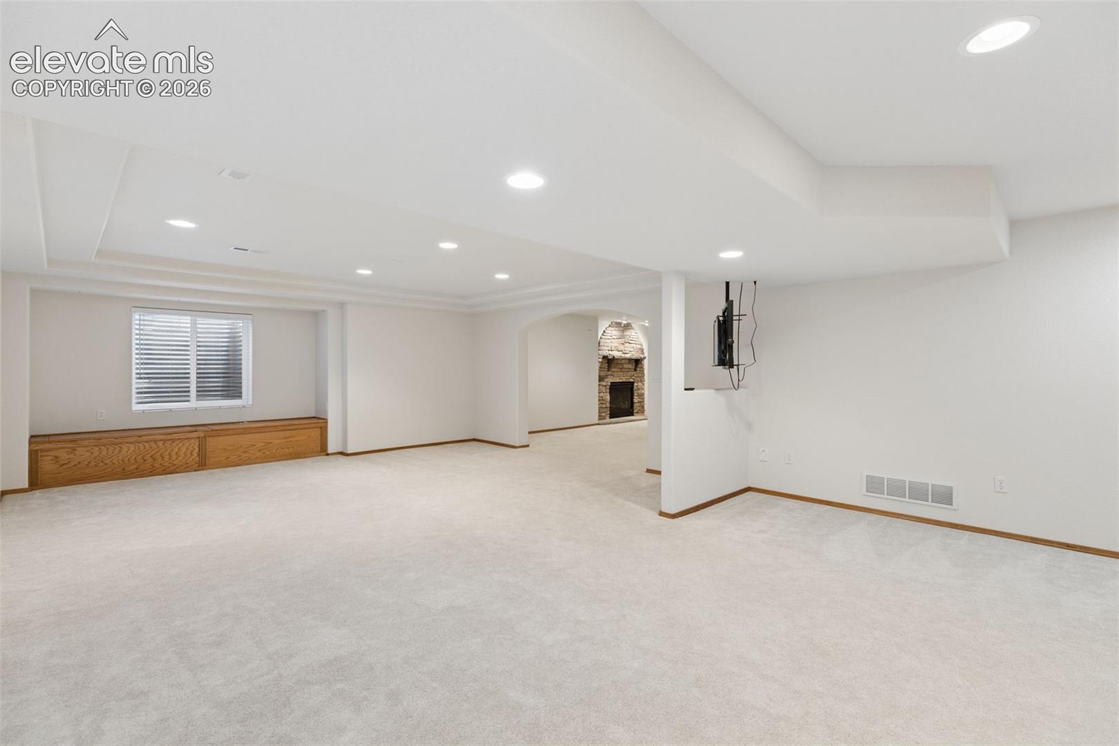 Open interior space featuring recessed lighting, a built-in wood-finish window bench, and a stone-accented fireplace