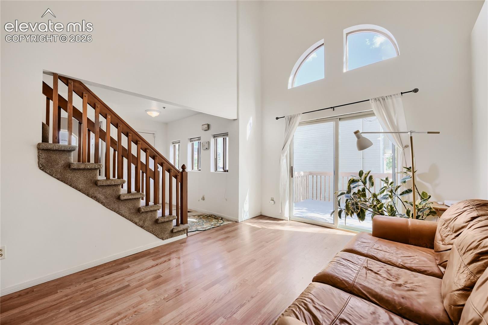 Bright, open foyer showcasing gleaming wood-finish flooring, a striking wooden staircase with detailed railings, soaring ceilings with transom windows, and abundant natural light from expansive glass doors and transom windows framing the outdoor space