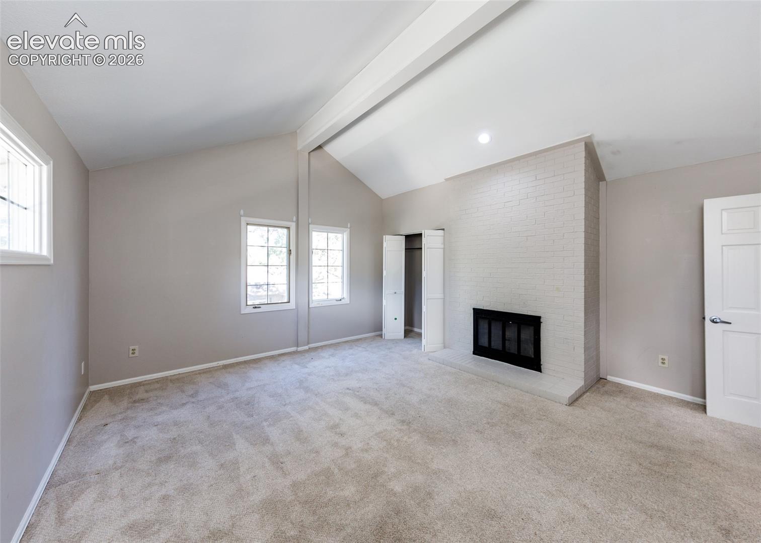 Vaulted ceiling with an exposed beam, white brick fireplace, and light-toned carpeting