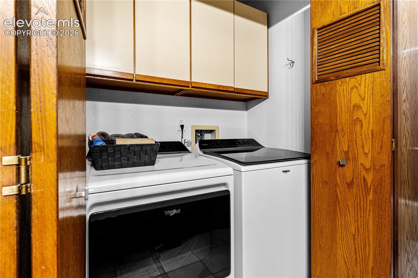 Utility room featuring overhead wood cabinetry and built-in wood-paneled door with integrated ventilation