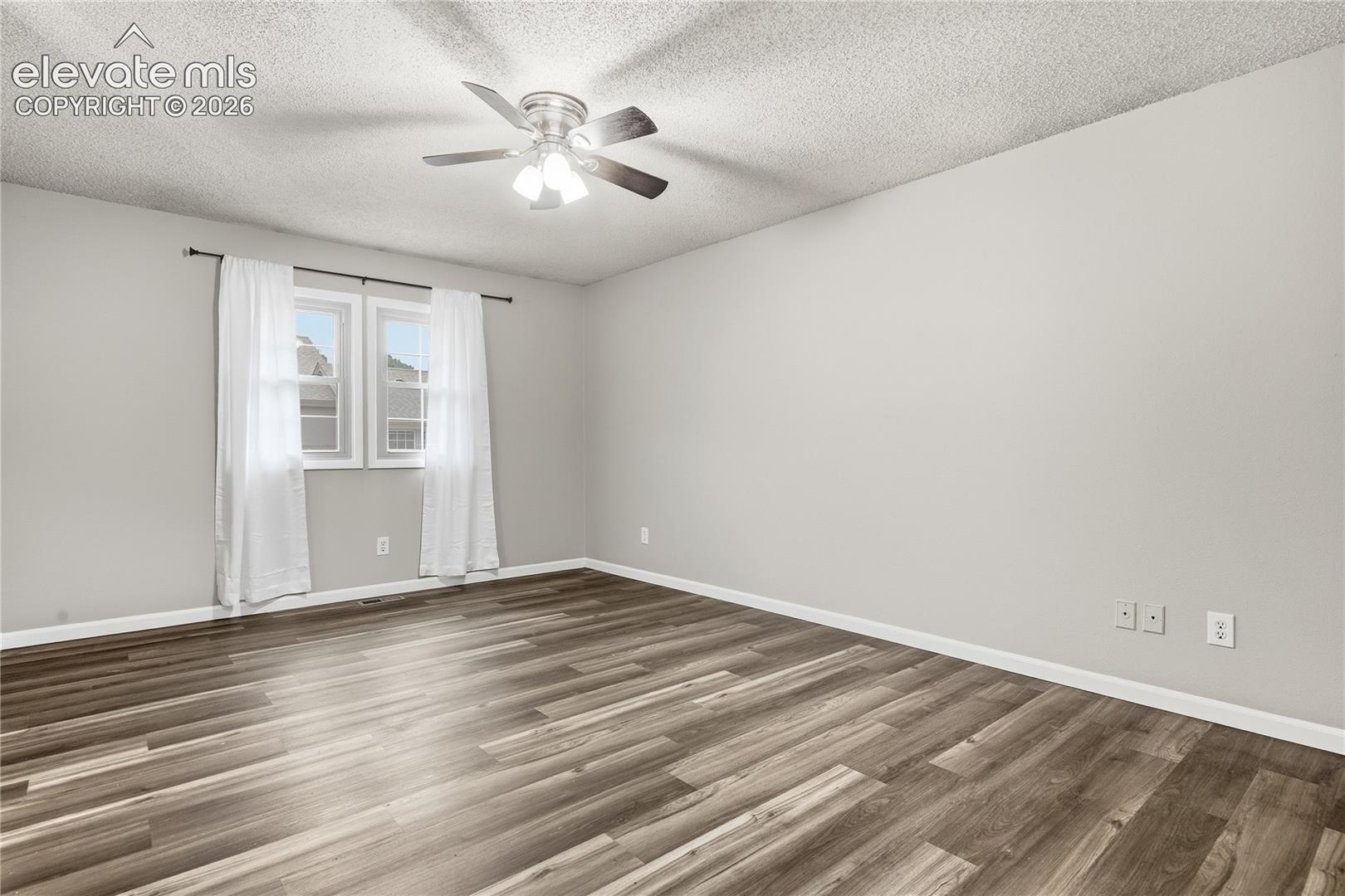 Wood-finish flooring, light neutral wall paint, two pane windows, and a ceiling fan with integrated lighting