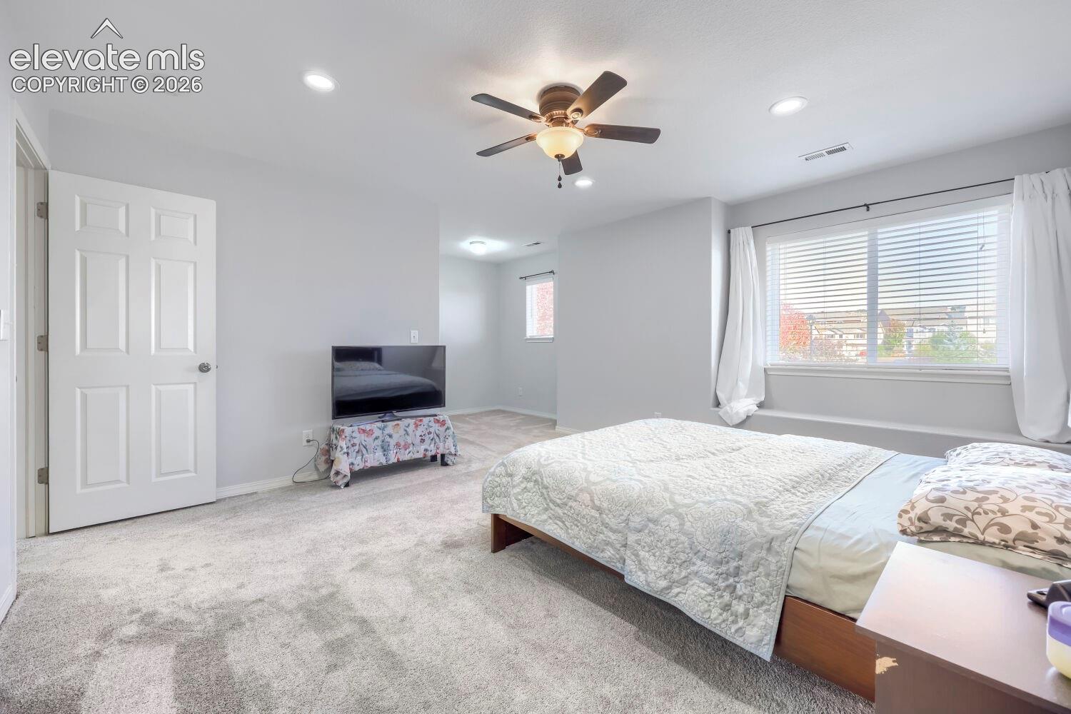 Neutral-toned interior space featuring recessed lighting, a central ceiling fan with integrated light, wall-to-wall carpeting, and a wide window with a deep sill