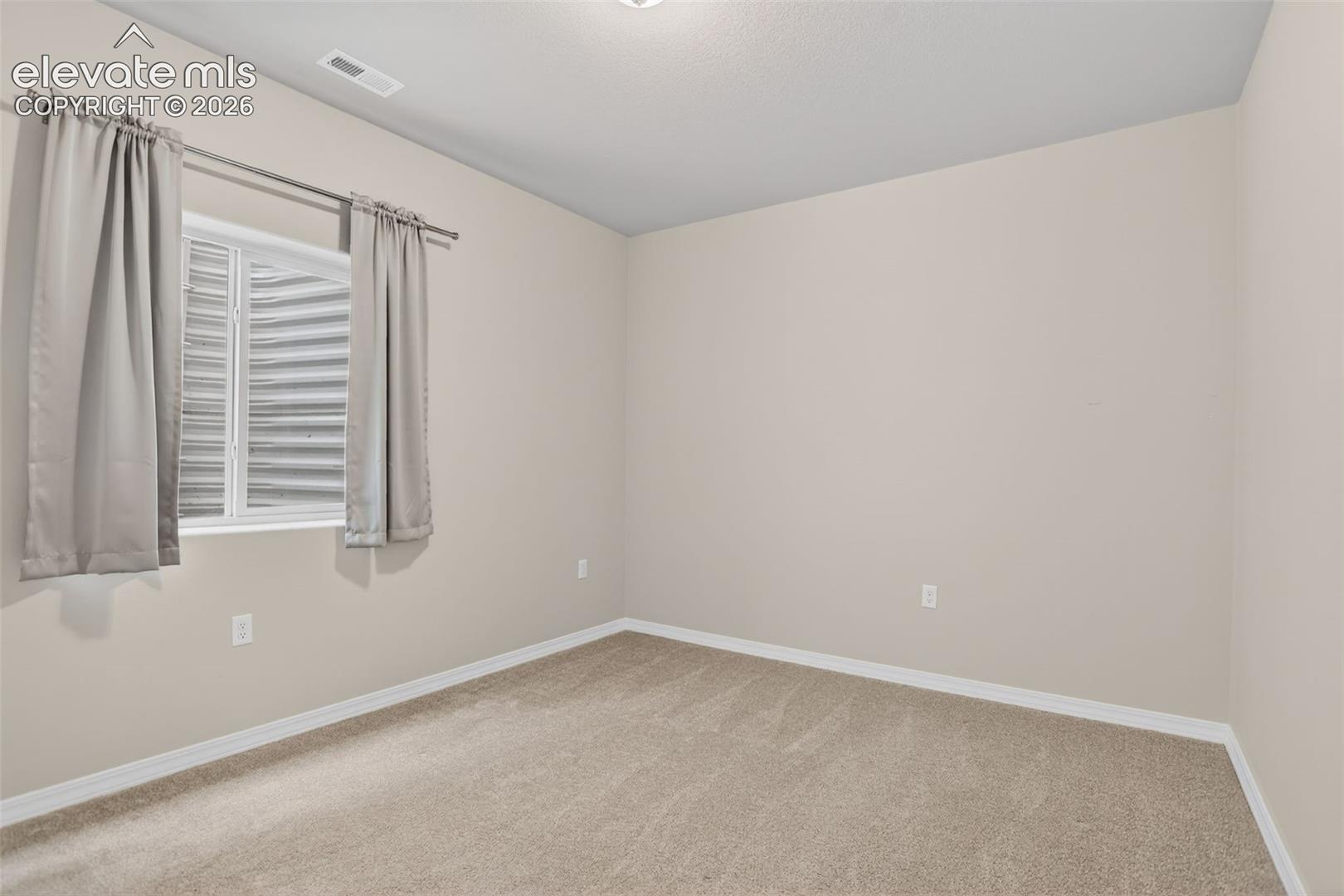 Neutral-toned room featuring a single window with a privacy screen, light beige carpeting, and white baseboards