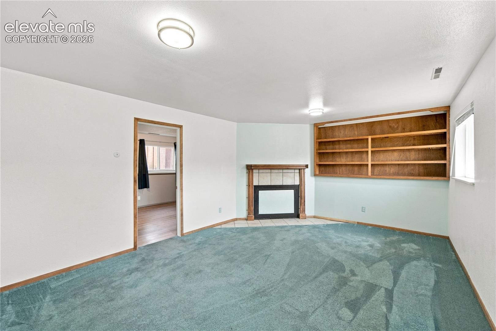 Built-in wooden shelving, recessed fireplace with tile surround, and overhead ceiling lighting