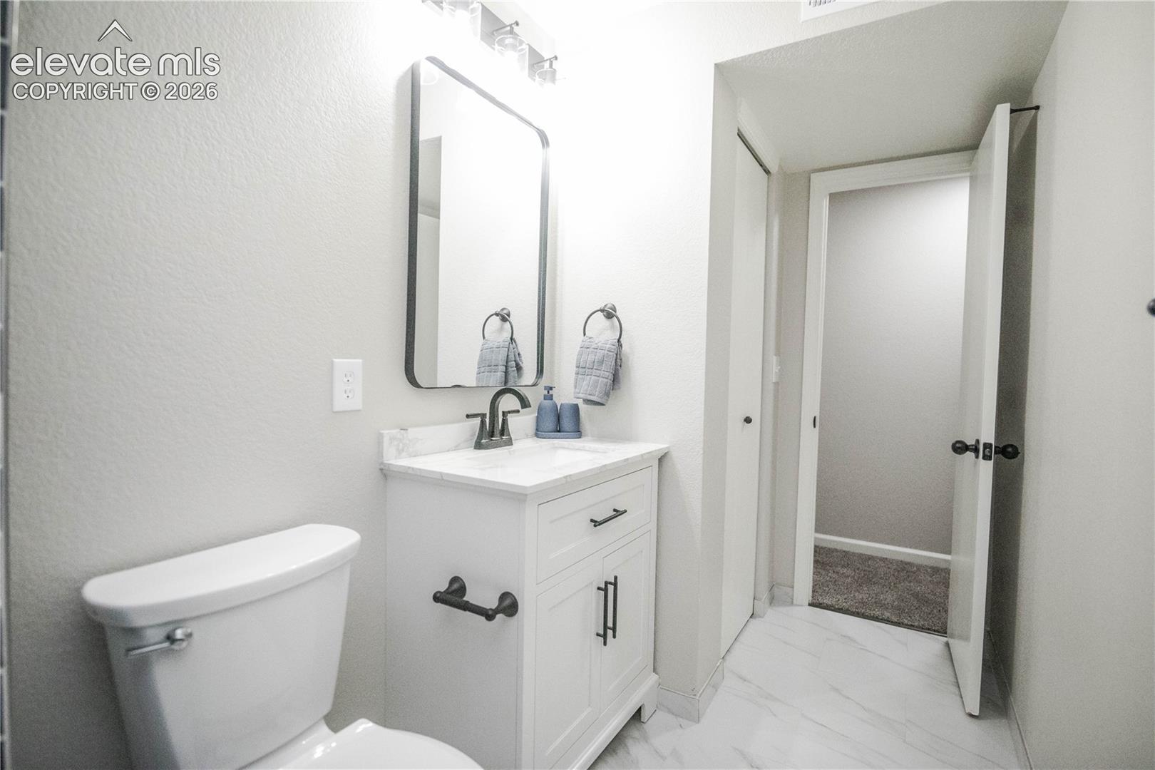 Bathroom featuring white cabinetry, stone-finish countertop with integrated basin, matte black hardware, and rectangular mirror