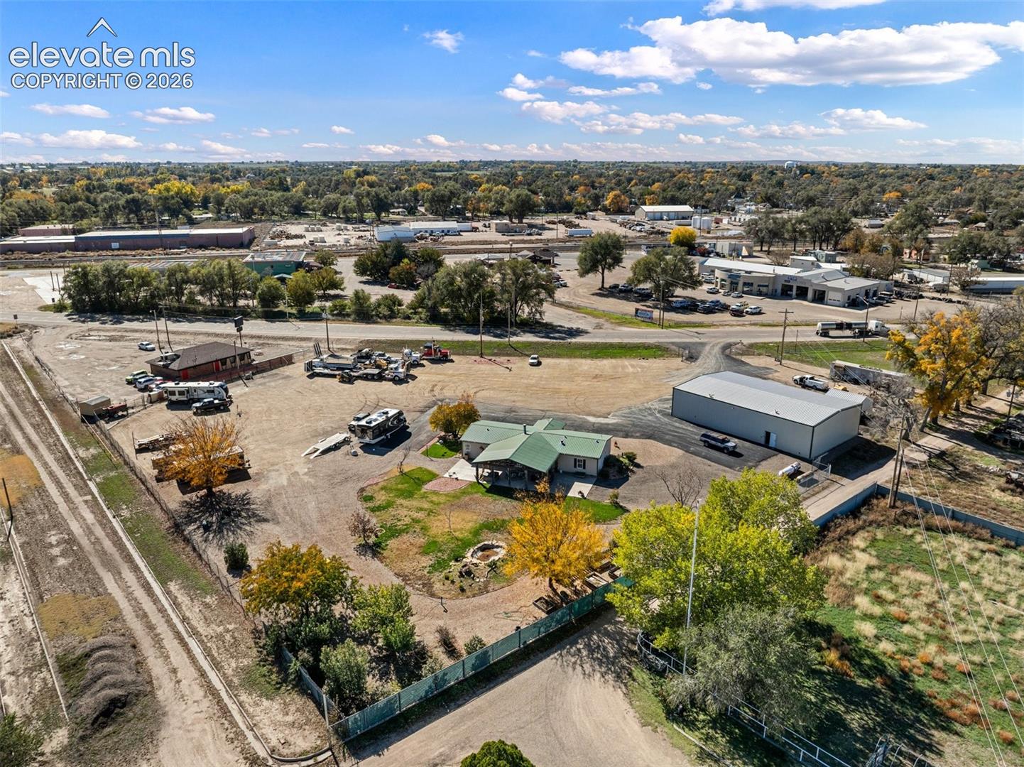 Aerial view of property featuring a detached metal structure, expansive graveled grounds, and mature perimeter trees