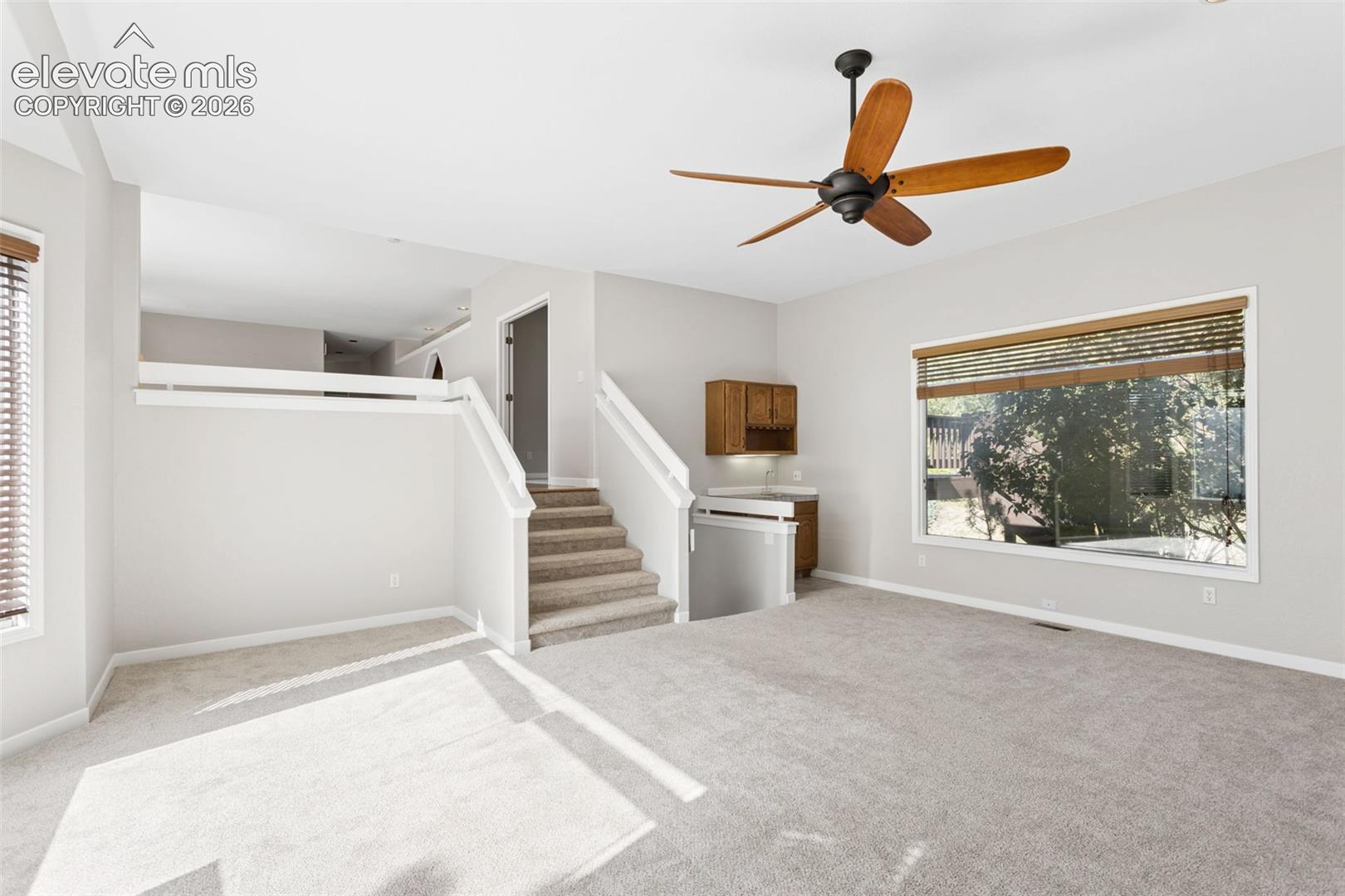 Carpeted room with a multi-level layout, featuring a built-in wet bar, a ceiling fan, and a large window
