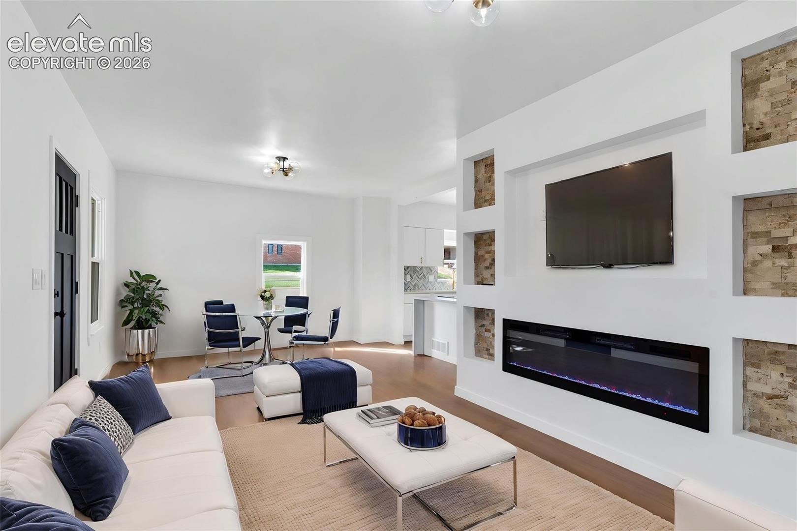 Linear electric fireplace with a stacked stone accent surround, built-in shelving niches, and wood-finish flooring