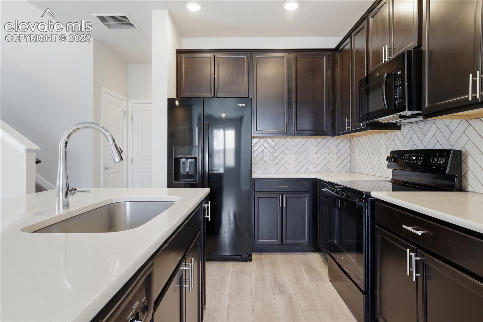 Kitchen featuring dark wood cabinetry, light-toned countertops, and a white herringbone-patterned backsplash