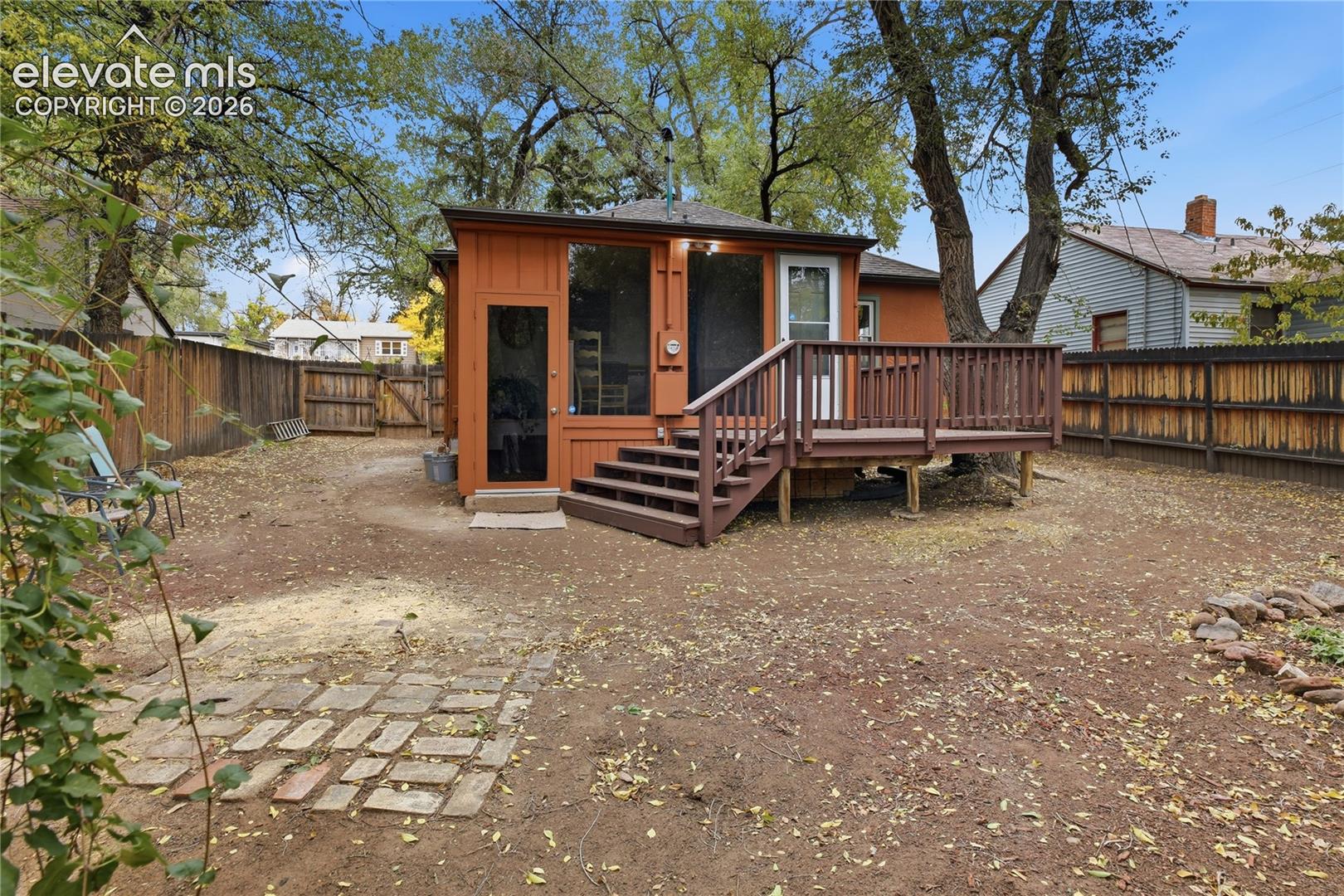 Backyard featuring an elevated wood deck, screened-in porch, stone paver path, and perimeter wood fencing