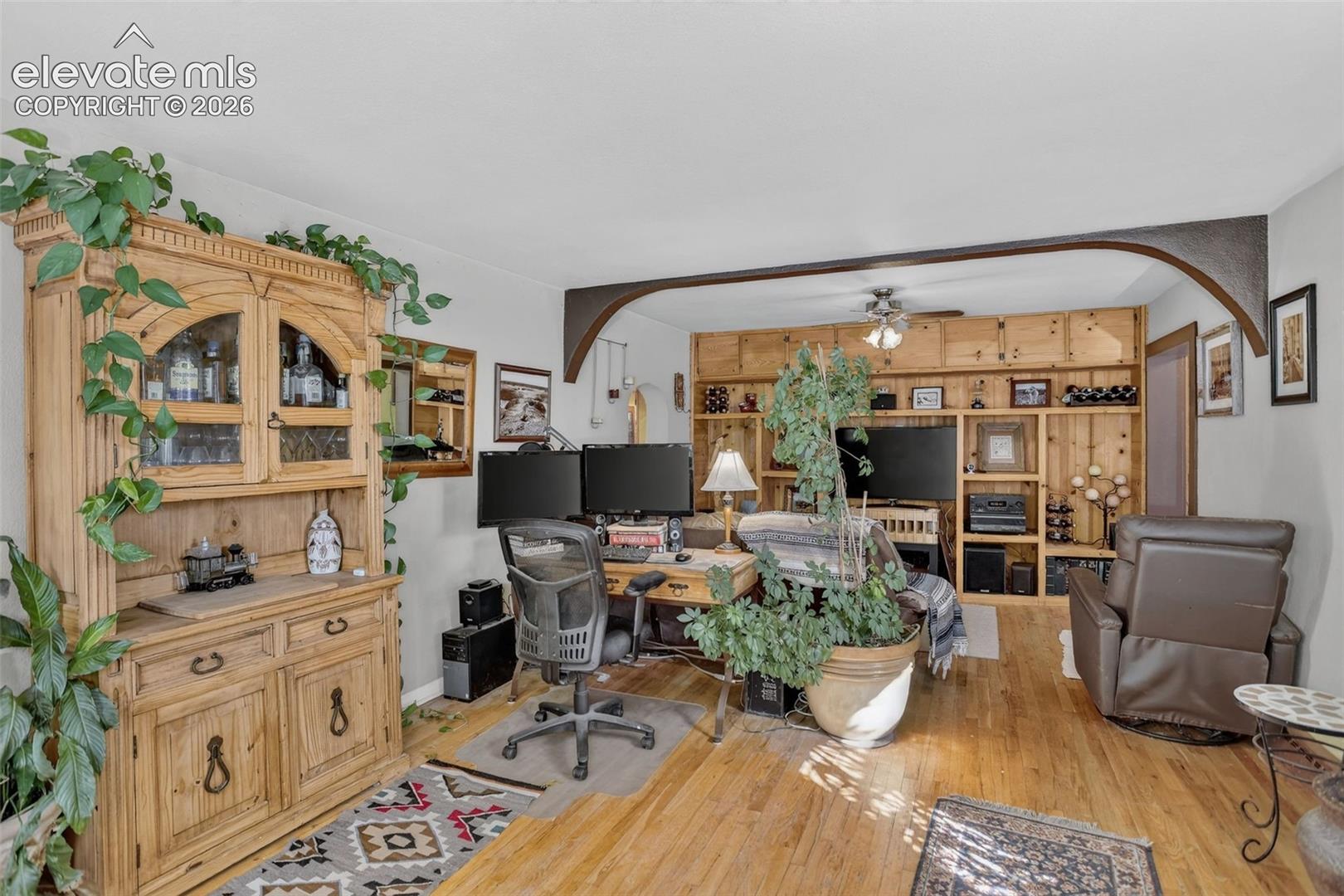 Hardwood flooring, arched entryway, built-in shelving, wood paneling, and ceiling fan