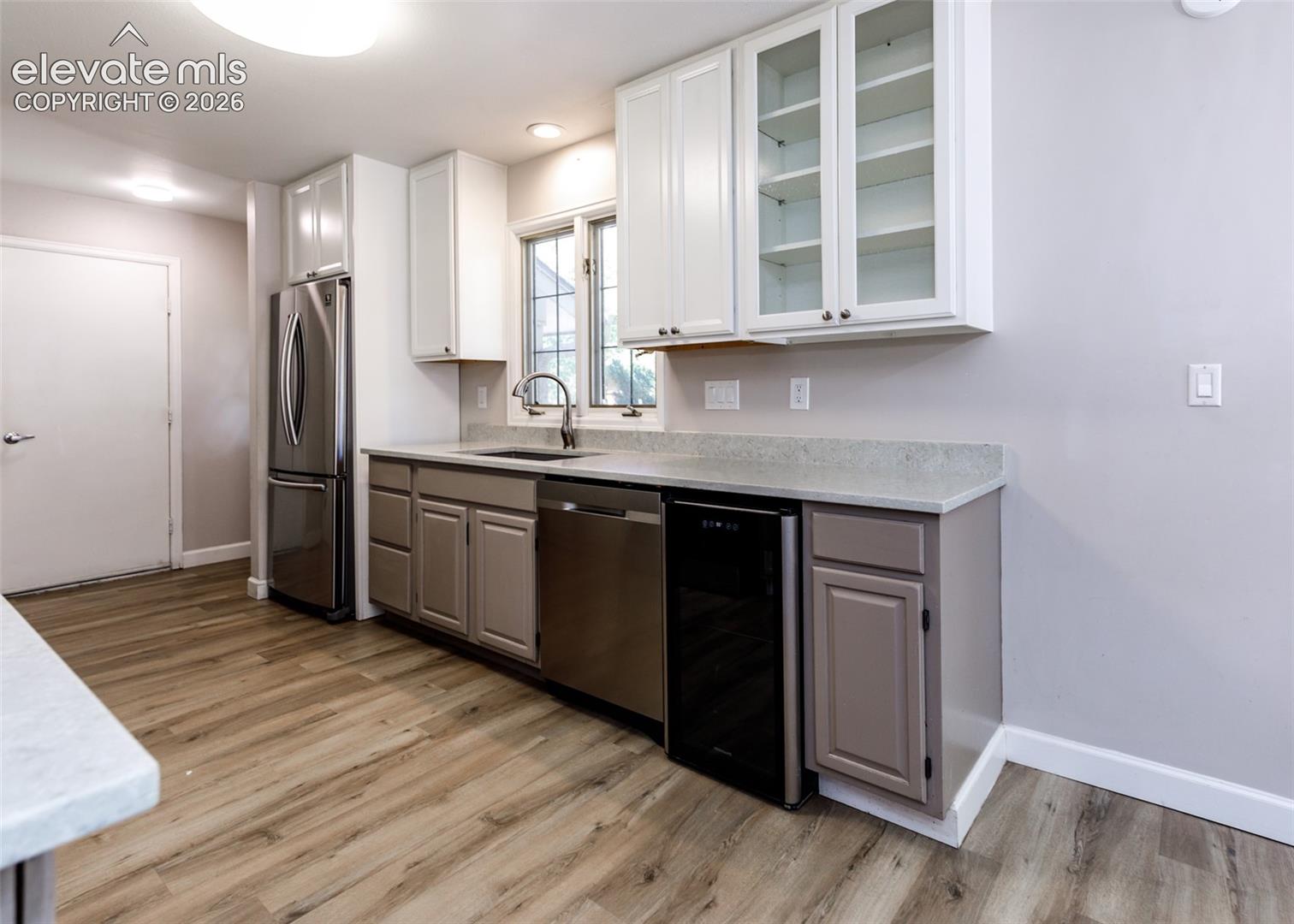 Kitchen featuring stainless steel appliances, light-toned wood-finish flooring, white upper cabinetry, gray lower cabinetry, and light speckled countertops