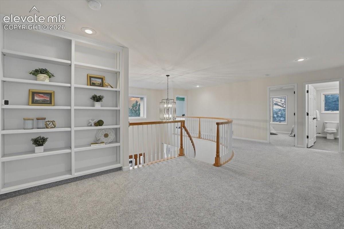 Built-in shelving, recessed lighting, curved wooden handrail, chandelier, light-colored carpet