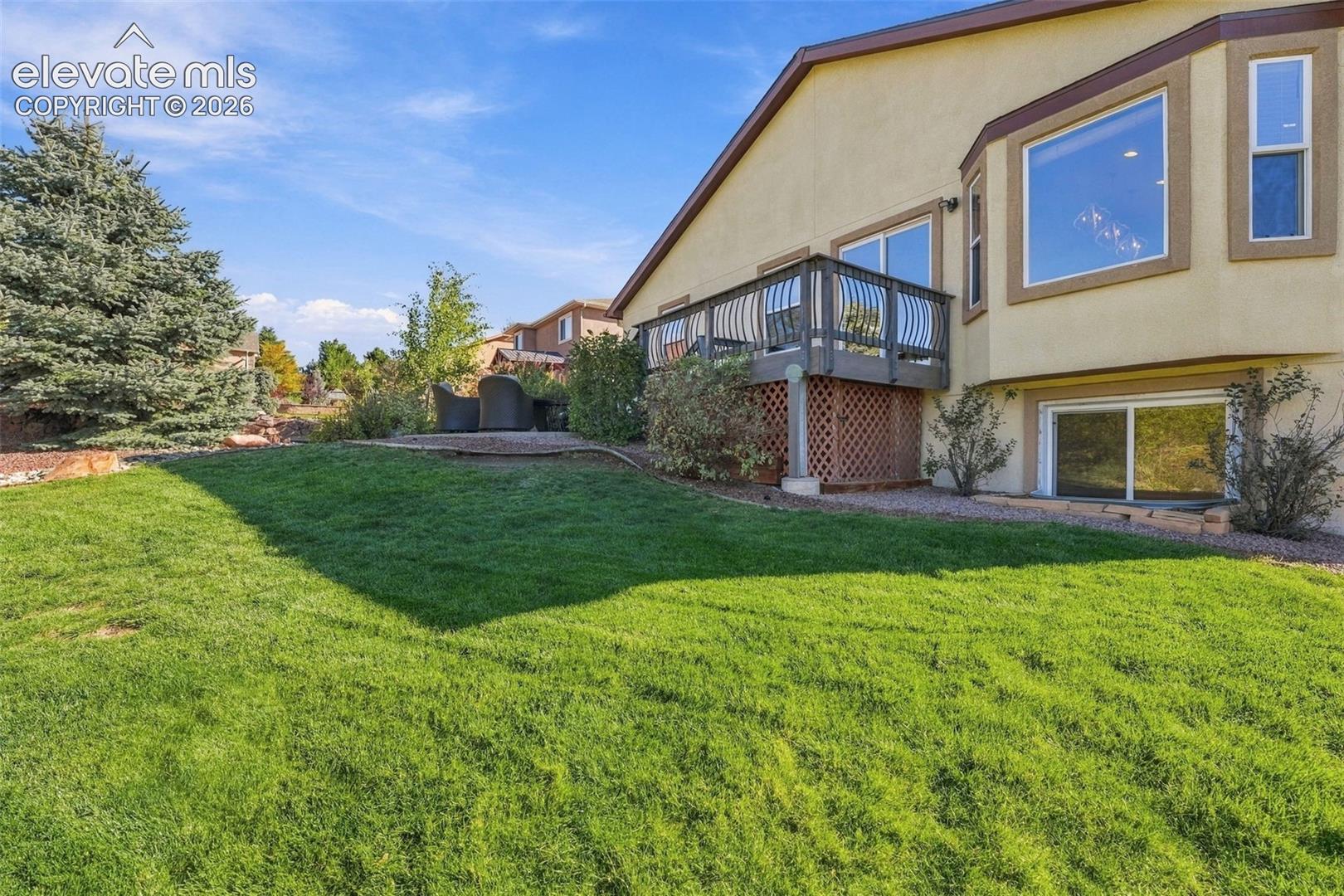 Backyard featuring a manicured lawn, elevated deck with metal railing, lattice skirting, and large window installations