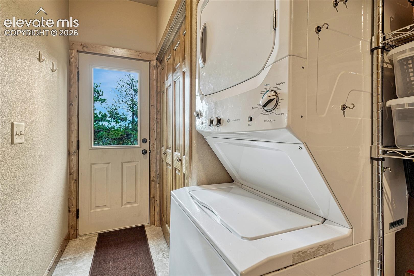 Dedicated utility area featuring stacked washer and dryer, wood-trimmed door with glass inset, and wood-finish cabinetry