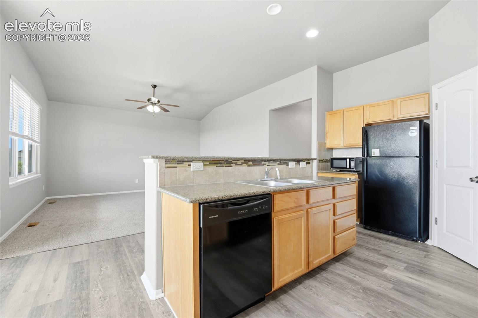 Kitchen with wood-finish flooring, light wood cabinetry, and black appliances