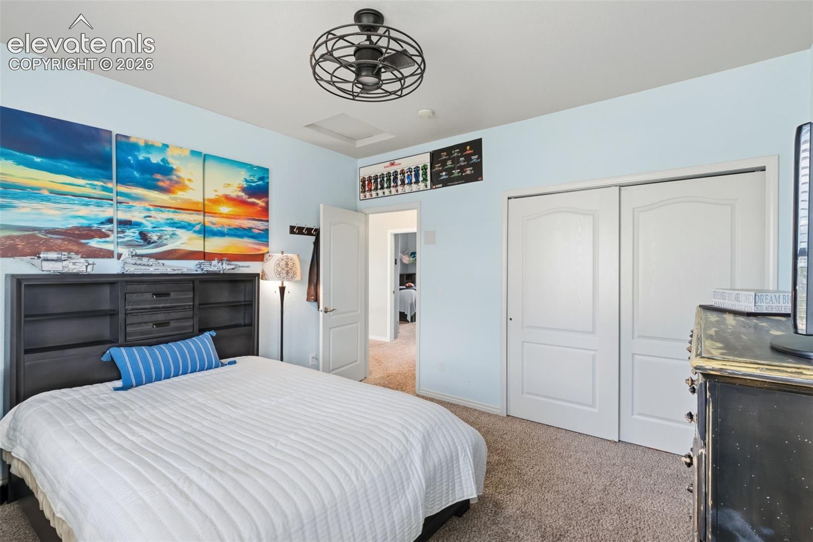 Carpeted bedroom featuring light blue walls, a ceiling-mounted fan fixture, and a built-in closet with double bifold doors